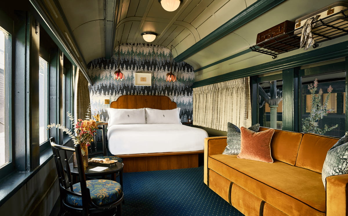 A white bed and orange couch with a black table and chairs inside the train room