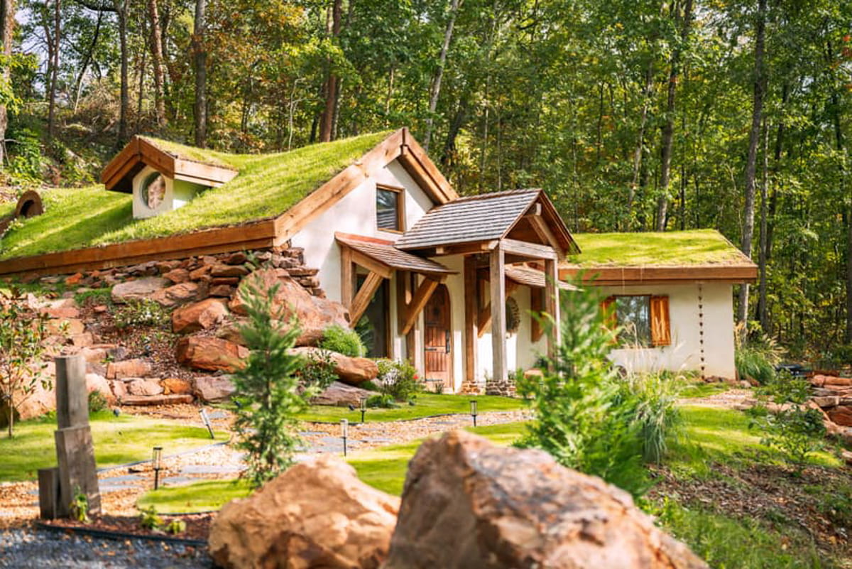 A white cottage with green moss on the roof and stone features on the outside